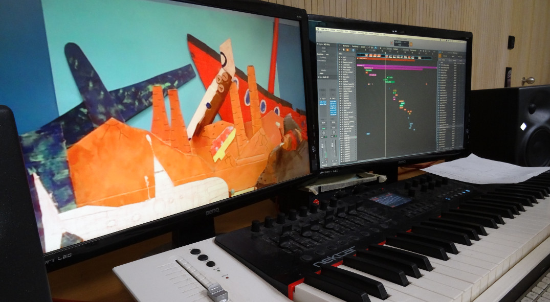 Zwei Monitore mit einem Standbild eines Trickfilms und der Oberfläche eines Videoschnittprogramms. Davor ein Keyboard zur Bearbeitung von Bild und Ton. 