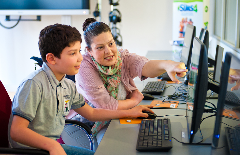 Mutter erklärt ihrem Sohn etwas und zeigt auf den Computerbildschirm.