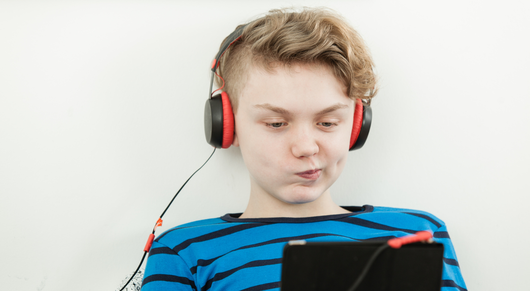 Junge mit Kopfhörer spitzt die Lippen während er auf sein Smartphone schaut