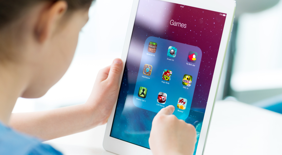 Mädchen klickt auf Tablet. Auf dem Display sind verschiedene Spiele-Apps zu sehen.