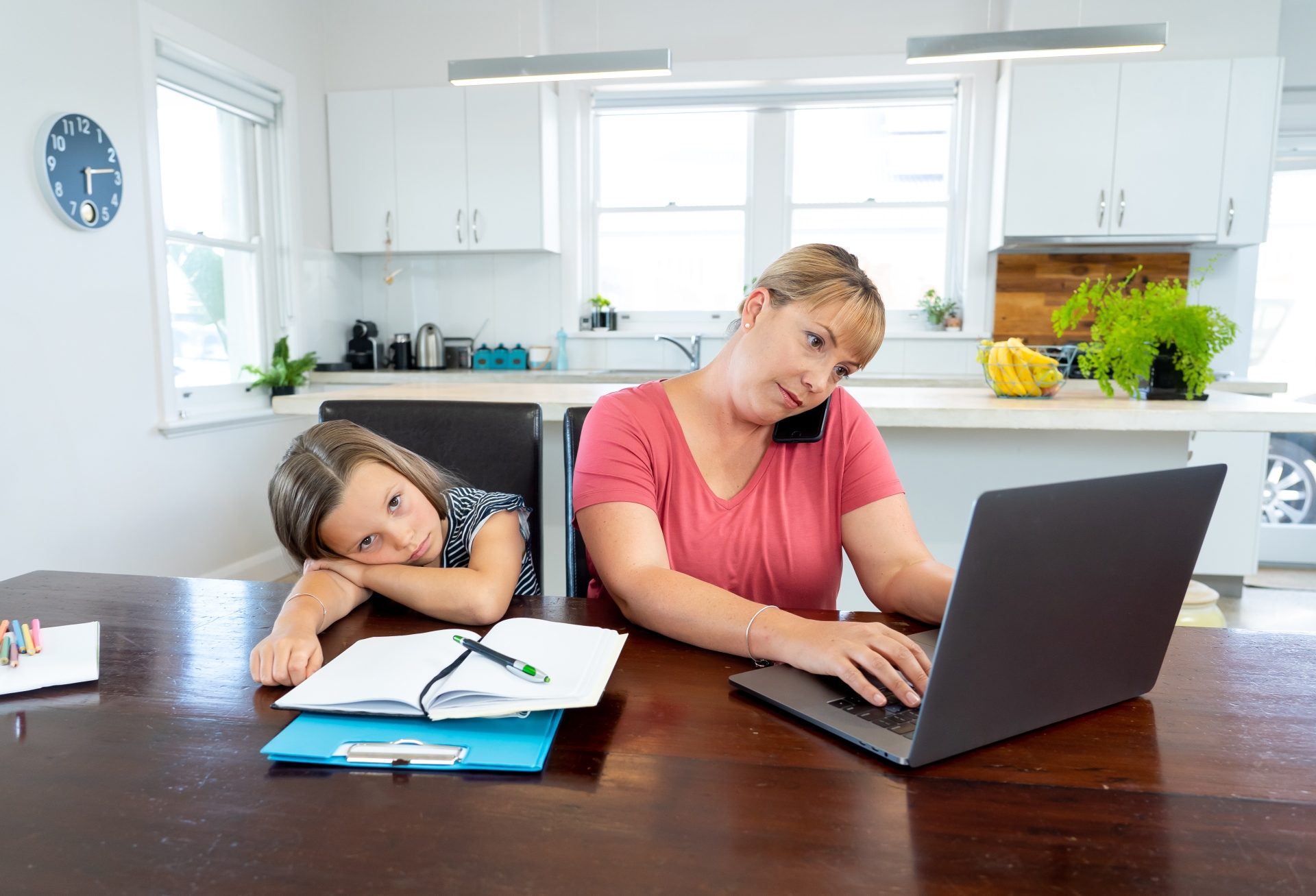 Mutter arbeitet am Laptop, Tochter sitzt müde und genervt daneben.