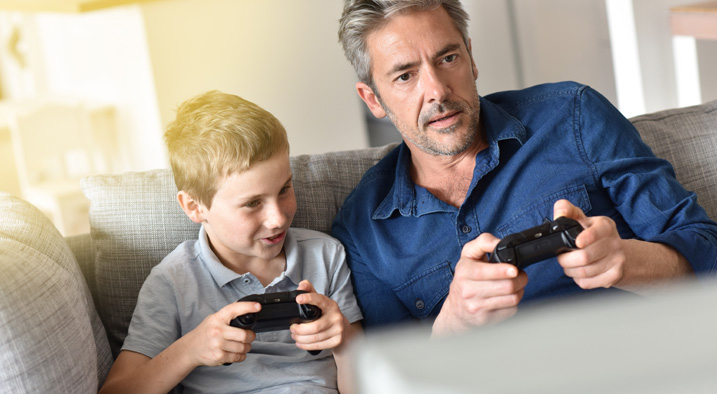 Vater und Sohn haben Controller in der Hand und spielen zusammen.