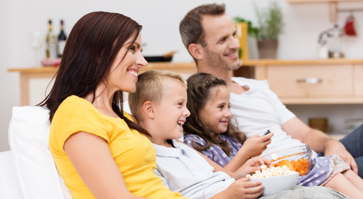 Vater, Mutter und ihre beiden Töchter sitzen auf der Couch beim Fernsehen.