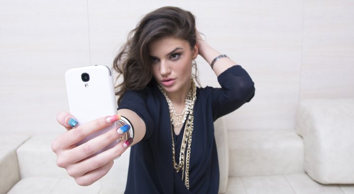 Junge attraktive Frau nimmt ein Selfie mit ihrem Smartphone und rückt ihre Haare zurecht.