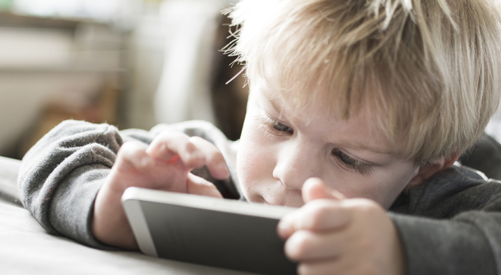 Kleiner blonder Junge klickt auf ein Smartphone.