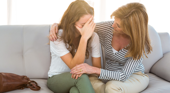 Junges Mädchen hält beschämt ihre Hand vors Gesicht und ihre Mutter tröstet sie.